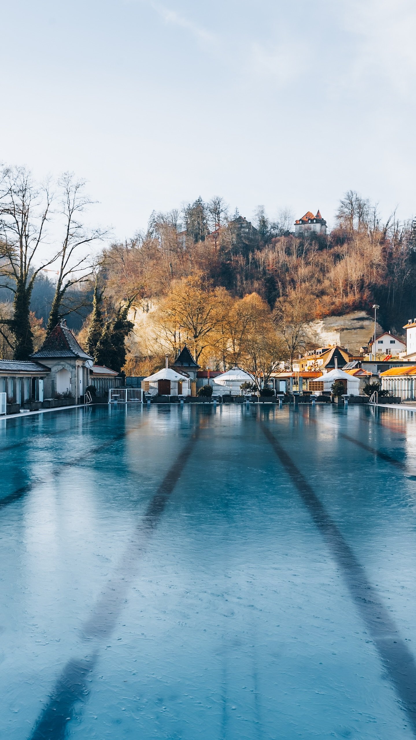 Le grand bassin des Bains de la Motta en hiver ; au fond, les yourtes blanches au pied des falaises et des arbres dorés