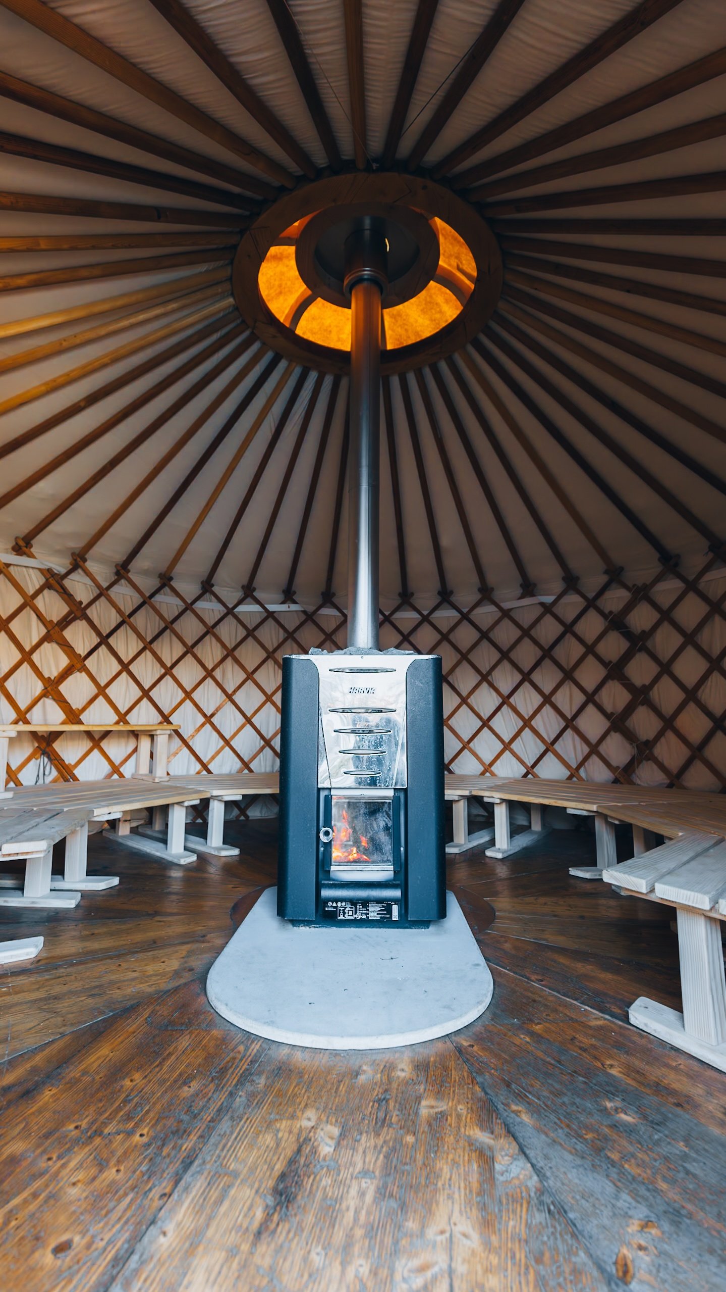 Intérieur d'une yourte-sauna : un poêle à bois allumé au centre et des bancs en cercle