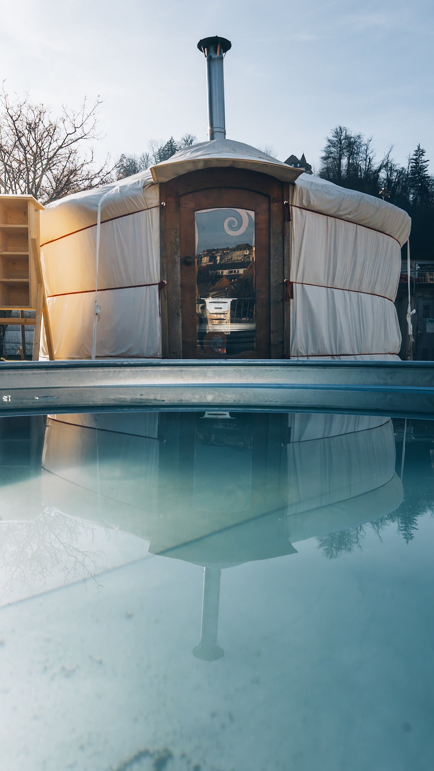 Une yourte-sauna se reflète dans l'eau turquoise d'un bassin froid